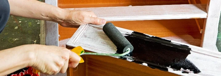 Person streicht Holzschrank mit Farbrolle schwarz